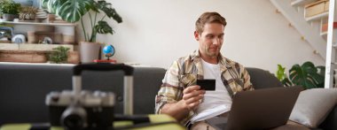 Mutlu adam portresi, gezgin, kredi kartı tutan ve dizüstü bilgisayar kullanan, tatil rezervasyonu yapan, yaz tatili için internetten bilet alan,.