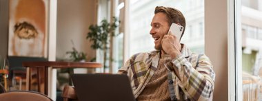 Kafe ziyaretçisi, dizüstü bilgisayarlı bir adam, telefonla arkadaşını arıyor. İş adamı telefonda konuşuyor, kahkahalarla gülüyor ve gülümsüyor..