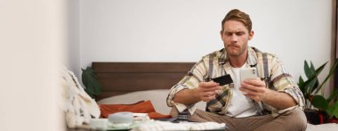 Bavuldaki mutlu adamın portresi, para transferi, internetten bilet alma, kredi kartı ve akıllı telefon uygulaması ile yatakta oturma, internet üzerinden ödeme..