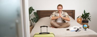 Genç, düşünceli bir adamın portresi, tatile çıkan turist, bavulunu toplayan, rahatlatıcı bir tatile hazırlanan, meditasyon yapan, dünya ile yatakta oturan, uçak biletleri ve kamera kayıtları..