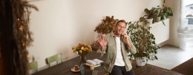 Gözlüklü yakışıklı genç adam, ofis masasında oturuyor, sana merhaba demek için el sallıyor, kameraya bakıyor, cep telefonuyla konuşuyor, bir telefon görüşmesi yapıyor..