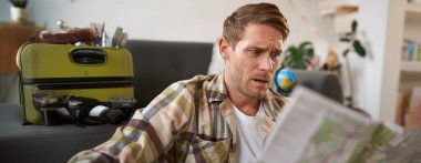 Seyahat haritasına bakan kafası karışık bir adamın portresi, rotayı seçen, tatile giden, tatile gitmeyi planlayan. Turizm konsepti