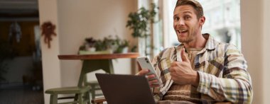 Mutlu kafe ziyaretçisi, genç serbest çalışan, kahve dükkanında çalışan, telefon ve dizüstü bilgisayarla oturan, başparmağını kaldıran ve evet diyen, güveni onaylayan, olumlu geri bildirim veren, ya da eleştiri yapan.