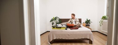 Tatile çıkan genç bir adamın portresi, bavulunu bir odaya topluyor, bavulla yatağa oturuyor, tatil için hazırlanıyor. Yaşam tarzı kavramı