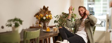 Kafedeki yakışıklı adam, kablosuz kulaklıkla müzik dinliyor, akıllı telefon çalma listesindeki favori şarkının tadını çıkarmak için kafeye bağlanıyor, oturup cappuccino içiyor..