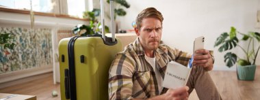 Kızgın adam bavuluyla oturuyor, cep telefonu ve pasaportu var. Seyahat konsepti