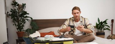 Bavuldaki mutlu adamın portresi, para transferi, internetten bilet alma, kredi kartı ve akıllı telefon uygulaması ile yatakta oturma, internet üzerinden ödeme..