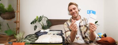 Yakışıklı bir genç adam resmi, turist iki uçak bileti ve pasaport gösteriyor, tatile çıkıyor, bavullarını hazırlıyor..