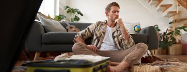 Stresli bir gencin bavulunu toplamasının portresi, tatilde ne giyeceğine karar vermesi, bavullara bakarken düşünmesi. Turizm konsepti