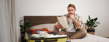 Bavullu bir adamın portresi, odada oturuyor ve notlarına ciddi ciddi bakıyor, tatil için hazırlanıyor, defterdeki eşyaların listesini kontrol ediyor. Boşluğu kopyala