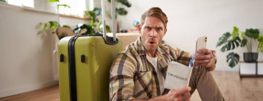 Adam kafası karışmış görünüyor, akıllı telefon kullanıyor, pasaport tutuyor, bagajın yanında oturuyor, seyahatini ya da tatilini planlıyor. Boşluğu kopyala