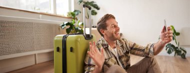 Mutlu turist portresi, uçuştan önce selfie çekiyor, bavullu fotoğraflar çekiyor, sosyal medyada resim yayınlamak için akıllı telefon kullanıyor..