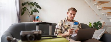 Huysuz adamın portresi, elinde biletler ve pasaport, dizüstü bilgisayar açıldı, endişeli ve sinirli görünüyor, bavuluyla koltukta oturuyor..