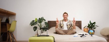 Yaz tatili için bavulunu topladıktan sonra yatakta meditasyon yapan genç bir adamın portresi, bacak bacak bacak üstüne atmış, nirvana pozu veren, rahatlatıcı, bir şeyler umut eden. Turizm ve farkındalık kavramı