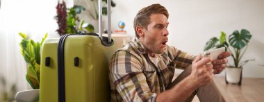 Bavullu bir adam, yerde oturuyor, telefon ekranına bakıyor. Turizm konsepti