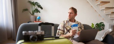 Huysuz adamın portresi, elinde biletler ve pasaport, dizüstü bilgisayar açıldı, endişeli ve sinirli görünüyor, bavuluyla koltukta oturuyor..