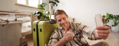 Mutlu genç adam onaylıyor, cep telefonundan selfie çekiyor, bavulun yanında poz veriyor, blogcu tatile çıkıyor ve tatille ilgili gönderiler yolluyor. Turizm konsepti