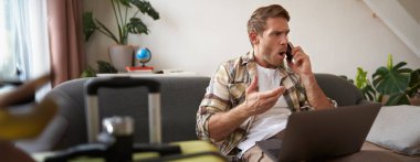 Telefonda tartışan öfkeli bir adamın portresi dizüstü bilgisayarı açık, bavulun yanında oturuyor, seyahat acentesine şikayet ediyor. Boşluğu kopyala