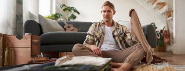 Stresli bir gencin bavulunu toplamasının portresi, tatilde ne giyeceğine karar vermesi, bavullara bakarken düşünmesi. Turizm konsepti