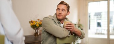 Kafedeki sandalyede oturan, kapuçino içen ve gülümseyen yakışıklı genç adamın portresi..