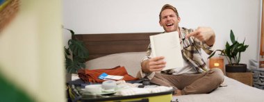 Seyahat ve turizm. Genç adam yatağa oturur, eşya listesini gösterir, defterini gösterir, giysilerini toplar, tatile çıkmaya hazırlanır, tatile gider, valizlerini toplar..