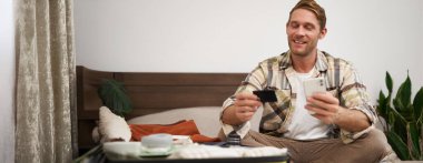 Gülümseyen adamın resmi bavulunu toplar, tatile hazırlanır, seyahat acentesinden seyahat satın alır, tatile gider, kredi kartı ve dizüstü bilgisayarla oturur. Yaşam tarzı ve turizm konsepti