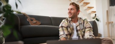 Bilgisayarı kullanan genç adamın portresini kapat, bilgisayara bak, yerde cihazıyla otur, web sitelerine bak.