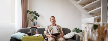 Genç bir adamın resmi, turist tatile çıkıyor, bavulunu hazırlıyor, dijital tabletle kanepeye oturuyor, okuyor, haritasına bakıyor, iş gezisi için kitap oteline gidiyor. Boşluğu kopyala