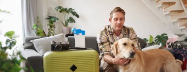 Genç bir adamın portresi, gezgin, köpeğini okşayan, bavul ve biletlerle oturan, tatile çıkan. Boşluğu kopyala