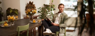 Bir kafede oturan, kahve içen, kablosuz kulaklık takan, müzik dinleyen veya halka açık alanda dijital tablet kullanan yakışıklı bir gencin hayat tarzı fotoğrafı..