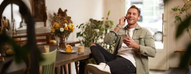 Karizmatik, gülümseyen genç bir adam, bir fincan kahveyle kafede oturup dinleniyor, müzik dinliyor ya da kablosuz kulaklıkla podcast yapıyor, akıllı telefon tutuyor..