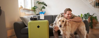 Tatile çıkan mutlu genç bir adamın portresi. Köpek arkadaşıyla seyahat ediyor. Golden Retriever 'la bavulların ve biletlerin yanında oturuyor..