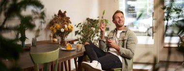 Gündelik giysiler içinde genç yakışıklı bir adamın portresi, kafede oturuyor ve en sevdiği şarkıyı seviyor, kablosuz kulaklıkla müzik dinliyor, kulaklıkla rahatlatıcı melodileri dinliyor, akıllı telefon tutuyor..