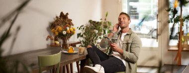 Yakışıklı, mutlu genç bir adamın portresi, bir kafede dinleniyor, kablosuz kulaklıkla müzik dinliyor, akıllı telefon tutuyor, en sevdiği şarkıyı çalıyor..