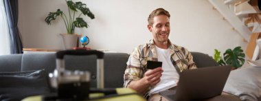 Mutlu adam internetten tatil rezervasyonu yapıyor, seyahat acentesinin internet sitesinden tatil parası ödüyor, internetten bilet alıyor, oturma odasında bavuluyla oturuyor..