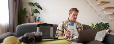 Sinirli adam uçak biletlerini tutuyor, dizüstü bilgisayara bakıyor, tatil turunda sorun yaşıyor..