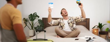 Mutlu gülümseyen bir adamın görüntüsü, neşeli turist dünya ve uçak biletleriyle oturur, tatile gider, bavuluyla oturur, seyahati için heyecanlanır, tatile çıkar. Turizm ve seyahat acentası kavramı