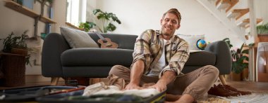 Genç bir adamın resmi, turist kıyafetleri bavulun içine sokmaya çalışıyor, tatil için hazırlanıyor. Turizm konsepti