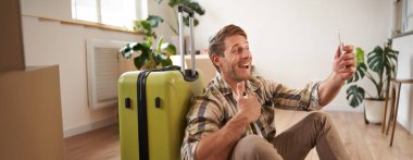 Mutlu turist portresi, uçuştan önce selfie çekiyor, bavullu fotoğraflar çekiyor, sosyal medyada resim yayınlamak için akıllı telefon kullanıyor..