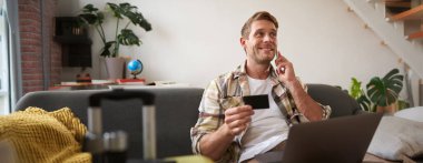 Gülümseyen adamın portresi, turist rezervasyon oteli, telefondan onay, kredi kartı ve dizüstü bilgisayar..