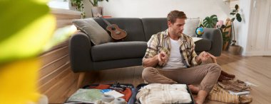 Tatilde ne getireceğine karar vermeye çalışan bir adamın portresi, bavulunu hazırlamak, panikle bagajına bakmak, tatile çıkmak. Turizm konsepti