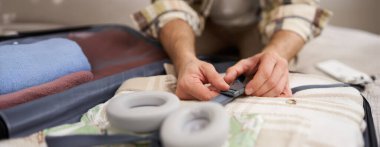 Erkek elleri kapalı, bavulun içine kıyafet bağlayan, eşyalarını bavula koyan, tatile çıkan, seyahat eden bir adam. Turizm ve seyahat kavramı