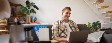 Laptoplu genç yakışıklı adamın portresi, pasaport ve iki uçak bileti hazırladı, bilgisayardaki yolculuğunu planladı, seyahat için oteller ve restoranlar ayarladı..