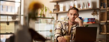 İnsan portresi üzgün ve stresli bir şekilde kahve bardağına bakar, kafeden çalışır, dizüstü bilgisayarla oturur, ilham kaynağı olmadan projeyi bitirmek için ilham vermez..
