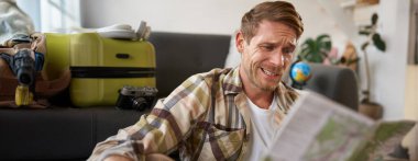 Elinde haritayla gülümseyen yakışıklı bir adam, bavulunu toplamış, tatile çıkıyor, tatile çıkmaya hazırlanıyor..