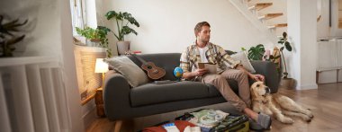 Köpeğiyle oturan bir adamın portresi, bayram için bavul hazırlıyor, evcil bir hayvanla geziye çıkıyor. Turizm konsepti