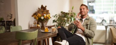 Kafedeki yakışıklı adam, kablosuz kulaklıkla müzik dinliyor, akıllı telefon çalma listesindeki favori şarkının tadını çıkarmak için kafeye bağlanıyor, oturup cappuccino içiyor..