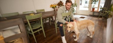 Kahve dükkanında siparişini bekleyen, bir köpeği okşayan, hayvan dostu bir kafede dinlenen yakışıklı genç adamın yakın portresi..