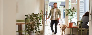 Yakışıklı, gülümseyen genç bir adamın tasmalı Golden Retriever köpeğiyle kafeye girişinin portresi. Adam evcil hayvan dostu kafeye giriyor..