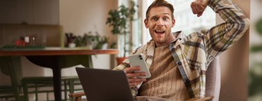 Komik bir sporcunun portresi, kafede oturan, dizüstü bilgisayarlı ve akıllı telefonlu sandalyede oturan, pazılarını esneten, kamerada kaslarını gösteren ve ne kadar güçlü olduğuyla övünen biri..